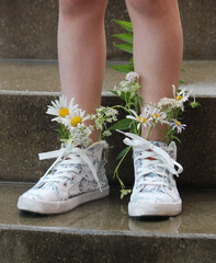 Naklejka premium Naked legs in white sneakers and with a bouquet of flowers are reflected in a puddle. Spring