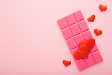 Pink chocolate bar and red bright hearts on light table background. Pastel color. Sweet snacks....