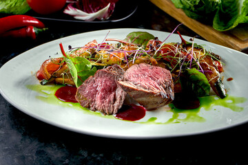 Medium rare beef medallions with vegetable garnish, served on a white plate. Dark marble background. Barbecue meat, restaurant food. Tasty steak