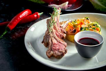 Rack of lamb medium rare with vegetable puree and berry sauce, served in a white plate. Dark marble background. Meat, restaurant food