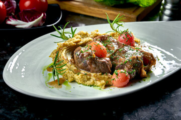 Close up view on Stewed Osso Buco steak with tomatoes, mashed potatoes served in a white plate on a dark marble background. Italian steak. Restaurant food