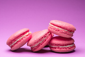 Colorful sweet macarons or macaroons, flavored cookies on purple background.