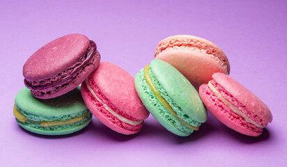 Colorful sweet macarons or macaroons, flavored cookies on purple background.