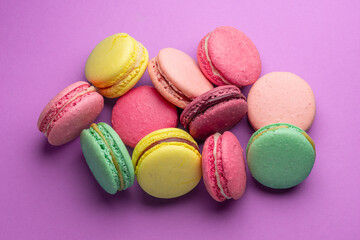 Colorful sweet macarons or macaroons, flavored cookies on purple background.