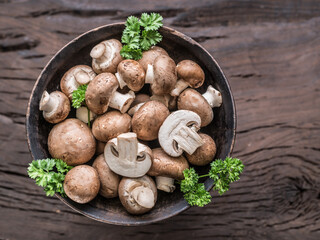 Different brown colored edible mushrooms in the wooden bowl on wooden table with herbs. Top view.