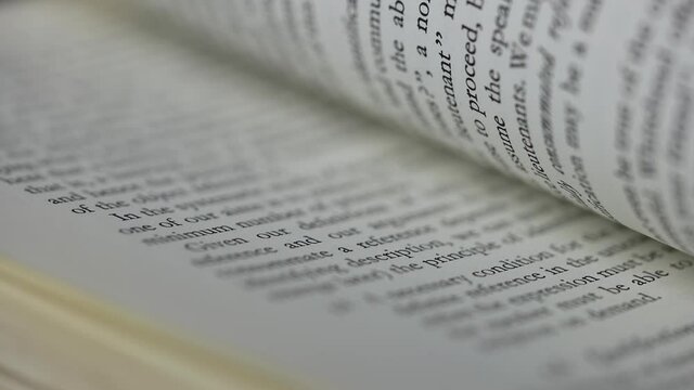 Open book close up. Macro shot of flipping white pages of a book with english text, side view. Part of the text is blurry. Slow motion.