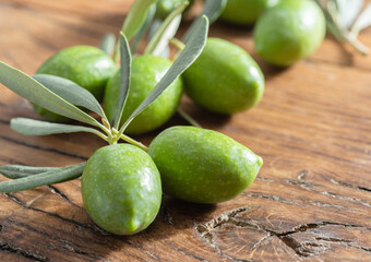 Green natural olives with olive leaves on a vintage old wooden table.