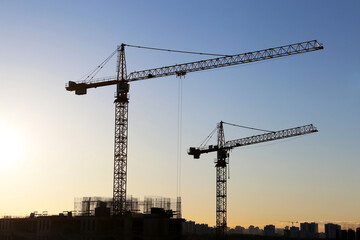 Silhouettes of construction cranes and unfinished residential buildings on sunrise background. Housing construction, apartment block in city