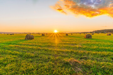 Scenic view at beautiful sunset in a green shiny field in willage farm with hay stacks, cloudy sky,...
