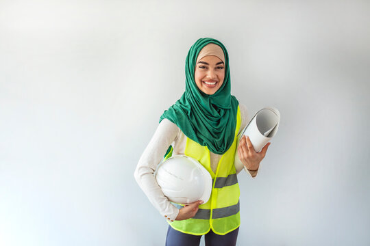 Portrait of female architect in hidjab. Smiling constructor worker muslim woman with clipchart and safety suit standing isolated on gray background. Portrait of Arab architects