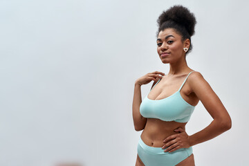 Playful young mixed race woman wearing blue underwear looking at camera, posing isolated over light background