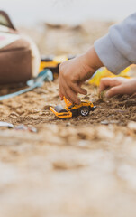 Manos de un chico joven jugando con vehículos de construcción en la arena