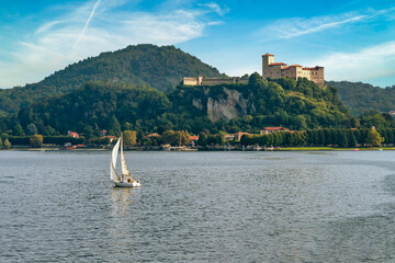 View of the Rocca di Angera with in the foreground a white sailboat sailing on Lake Maggiore, Italy