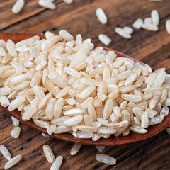 Brown rice raw long grain in a spoone, wooden background close up