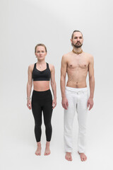 Fototapeta na wymiar A man and a woman stand next to each other shoulder to shoulder before a yoga workout. Couple of young people in sportswear in studio on white background.