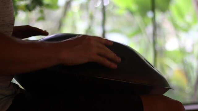Medium shot of a man playing a hang drum or hand pan instrument