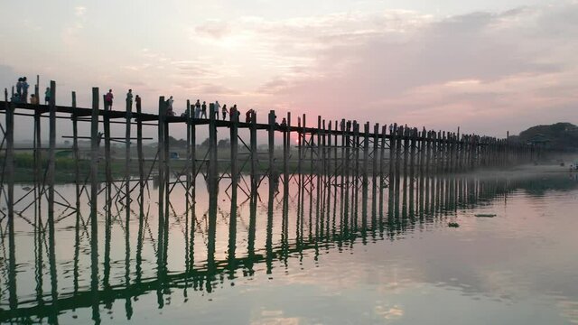 U Bein bridge with red sunset behind revealing traditional boats in river