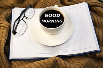 A white coffee cup with good morning written on it. Jacket with notepad and eyeglasses