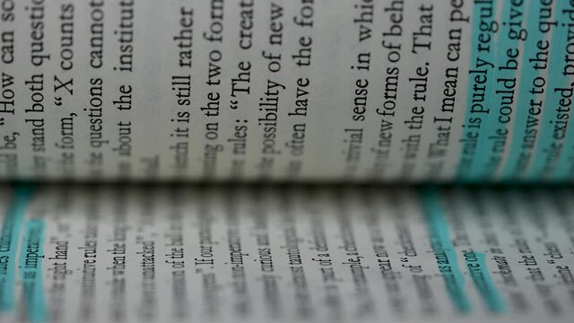 Flipping of white pages with English text in slow motion. The main theses from the book are highlighted in blue marker. Part of the text is blurry. Education concept. Close up.