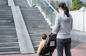 An Asian mother pushes a pram while her son sits in it