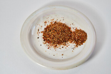 A scattering and a hill of small peppers and spices on a white plate and a white background