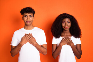 Photo of young happy positive good mood thankful afro couple hold hands chest isolated on orange color background