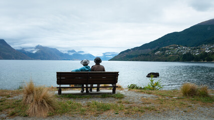 A couple sitting on the bench, enjoying the views of Lake Wakatipu and mountain ranges of Queenstown, South Island