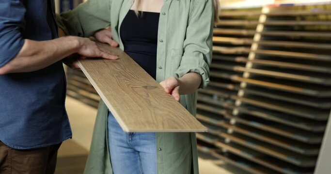 Young Couple Choosing Wood Texture Laminate Floor For Home Repairs In Flooring Shop