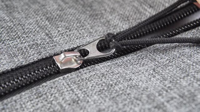 Metallic zipper bag in gray fabric. Plastic black teeth. Macro shot. Hand pulls the cord