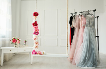 white wardrobe, large white strap, beautiful dresses in pastel colors hang on the hanger. Next to it, a rope entwined with beautiful, intense flowers.