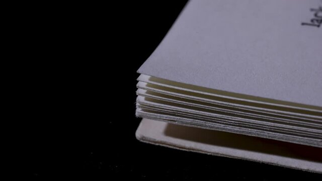 In a dark studio, a book is laid and opened on a black table, the pages are turned from beginning to end, then the book is closed and removed from the table. Close up corner of a book. Slow motion.