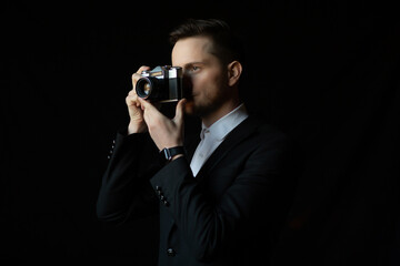 Fototapeta premium Elegant photographer wearing a suit is holding a vintage camera over black background.