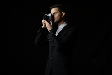 Bearded man wearing a classic suit holding a retro camera, making a photo. Photographer man uses camera.