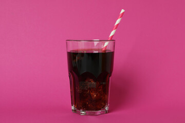 Glass of cola with ice cubes and straw on pink background