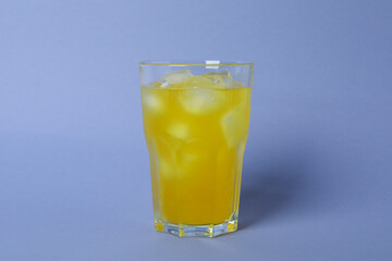 Glass of orange soda with ice cubes on violet background