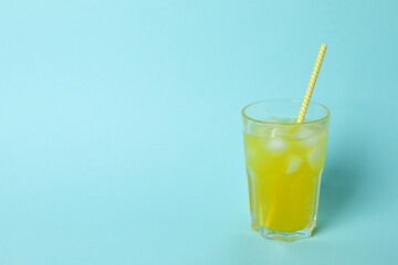 Glass of orange soda with ice cubes and straw on blue background