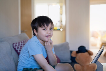 Portrait Active kid bitting his finger nails while looking at camera.Happy kid having fun watching cartoon or play game on tablet, Home schooling, Home learning or E-learning online education