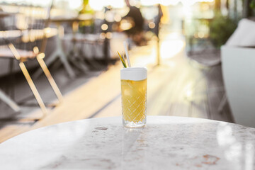 A long yellow sour cocktail in a tall glass with exotic decoration on a rooftop terrace