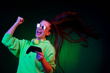 Photo of lucky woman dressed green pullover earphones dark glasses rising fist playstation isolated...