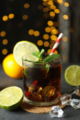 Glass of Cuba Libre on gray textured table against blurred lights