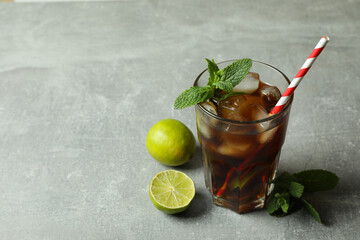 Glass of Cuba Libre and ingredients on gray background