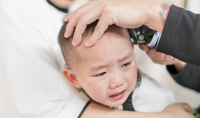 Obraz na płótnie Canvas Asian mothers with their sons in their arms are having their hair cut