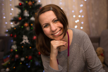 Portrait of a smiling woman at christmas time. Blurred decorated Christmas tree and glowing garland on the background.