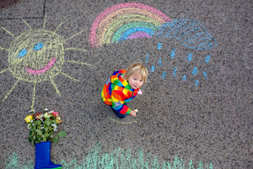 Cute toddler. playing in the rain with chalks, drawing on the asphalt, having fun