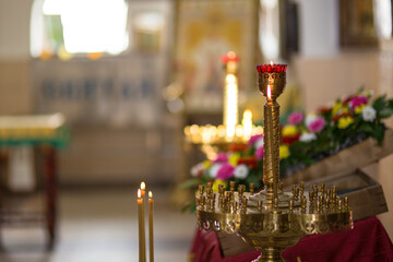 Naklejka premium Beautiful brass candlestick with burning candles in a Christian church. Colorful blurred background