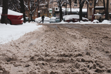 Close up of dirty snow on the city street; winter cityscape background.
