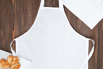 White apron template on brown wooden table with cookies, copy space. Kitchen, cooking clothing mockup