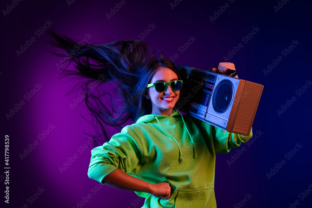 Sticker photo of charming cheerful young woman hold shoulder boombox fly hair smile isolated on dark gradien