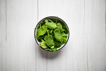 Fresh spinach leaves in bowl on rustic wooden table. Top view.