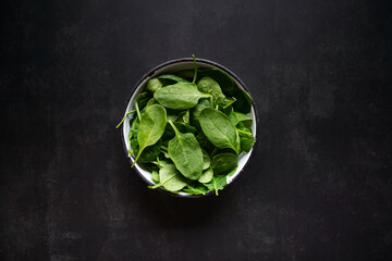 Fresh spinach leaves in bowl on rustic black table. Top view.